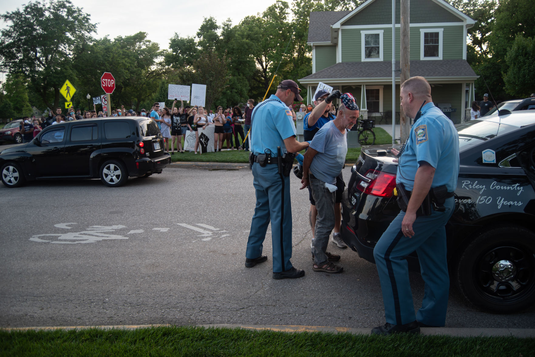 Riley County Police Officers escort a man from his front porch to a police cruiser after he was reported for being racist towards peaceful protesters before and after the gathering in Triangle Park on Tuesday.